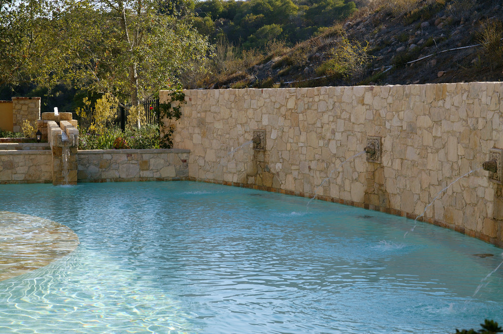 Diseño de piscina con fuente natural mediterránea grande redondeada en patio trasero con adoquines de piedra natural
