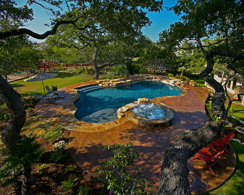 Diseño de piscina con fuente natural rústica de tamaño medio a medida en patio trasero con suelo de hormigón estampado