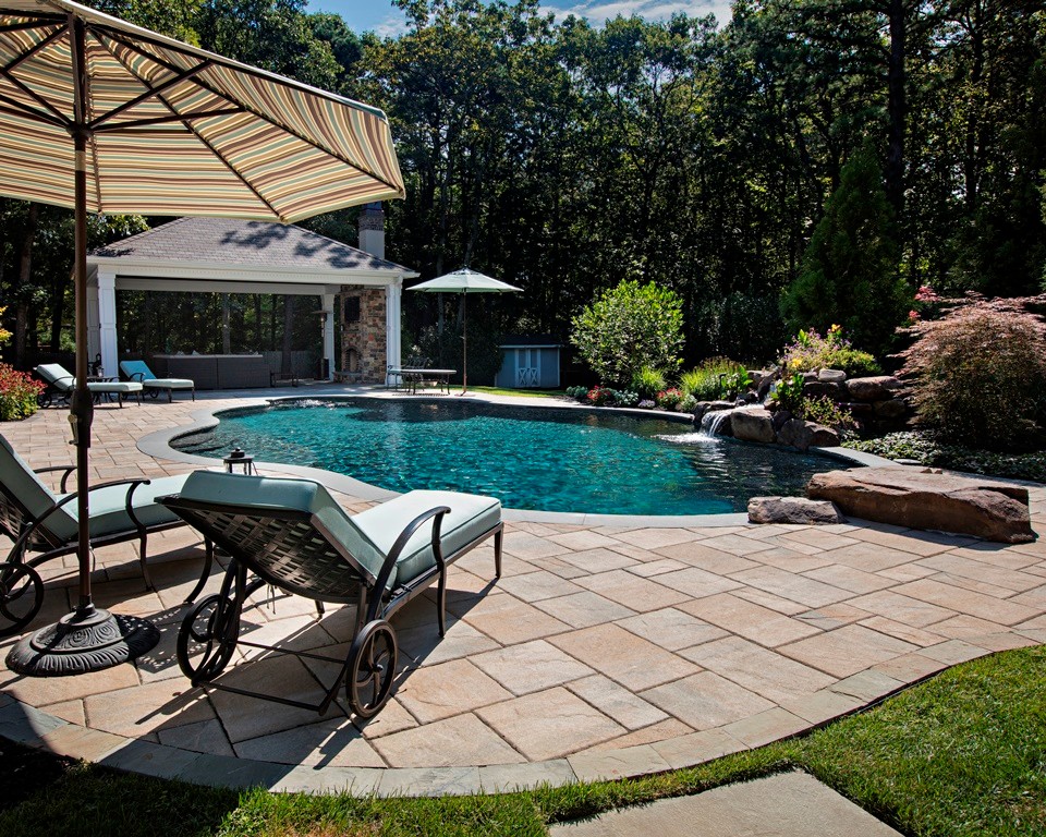 Réalisation d'un grand Abris de piscine et pool houses arrière tradition sur mesure avec des pavés en pierre naturelle.