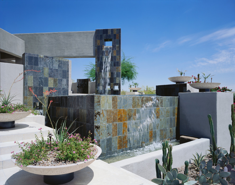 This is an example of a large contemporary back l-shaped infinity swimming pool in Phoenix with a water feature and tiled flooring.