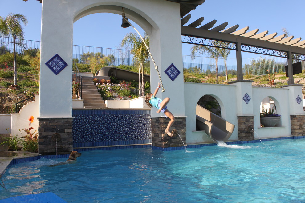 Ejemplo de piscina con tobogán mediterránea grande a medida en patio trasero