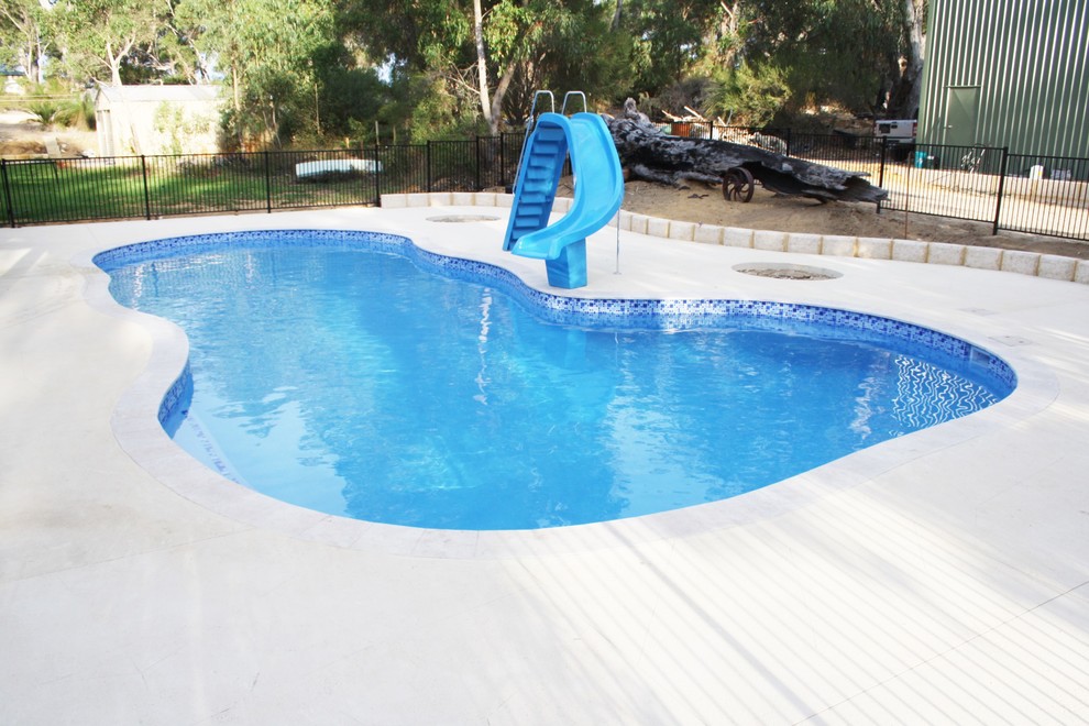 Idee per una grande piscina naturale country personalizzata dietro casa con un acquascivolo e lastre di cemento