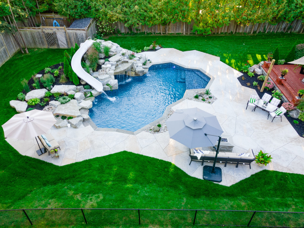 Modelo de piscina natural clásica renovada de tamaño medio a medida en patio trasero con paisajismo de piscina y suelo de hormigón estampado