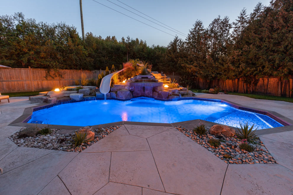 Modelo de piscina natural tradicional renovada de tamaño medio a medida en patio trasero con paisajismo de piscina y suelo de hormigón estampado