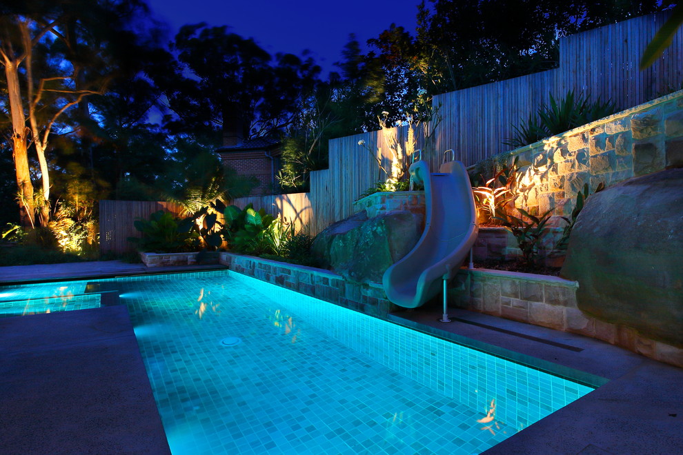 Diseño de piscina con tobogán alargada actual de tamaño medio rectangular en patio lateral con losas de hormigón