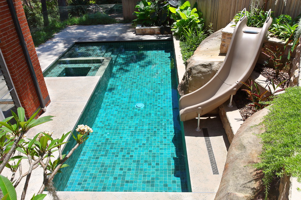 Foto de piscina con tobogán alargada actual de tamaño medio rectangular en patio lateral con losas de hormigón