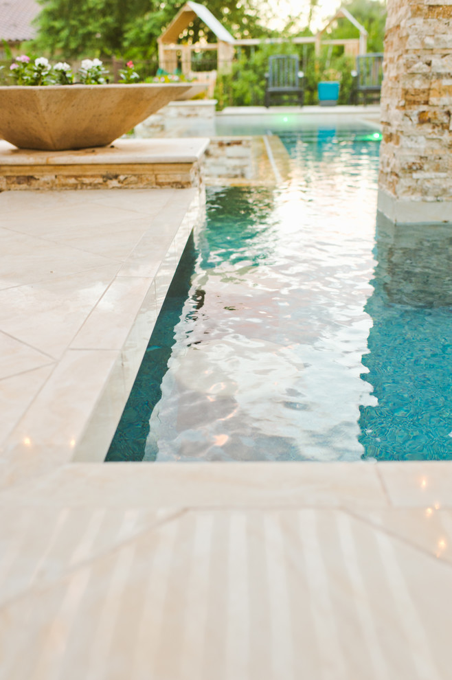Modelo de piscina infinita actual grande a medida en patio trasero con adoquines de piedra natural