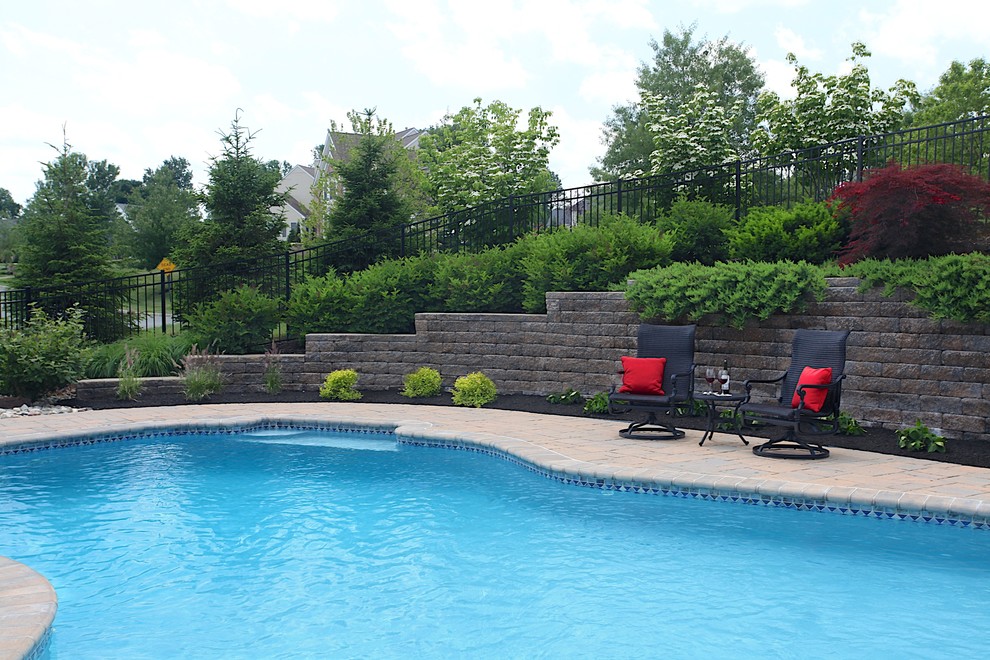 This is an example of a medium sized traditional back custom shaped swimming pool in New York with a water feature and concrete paving.