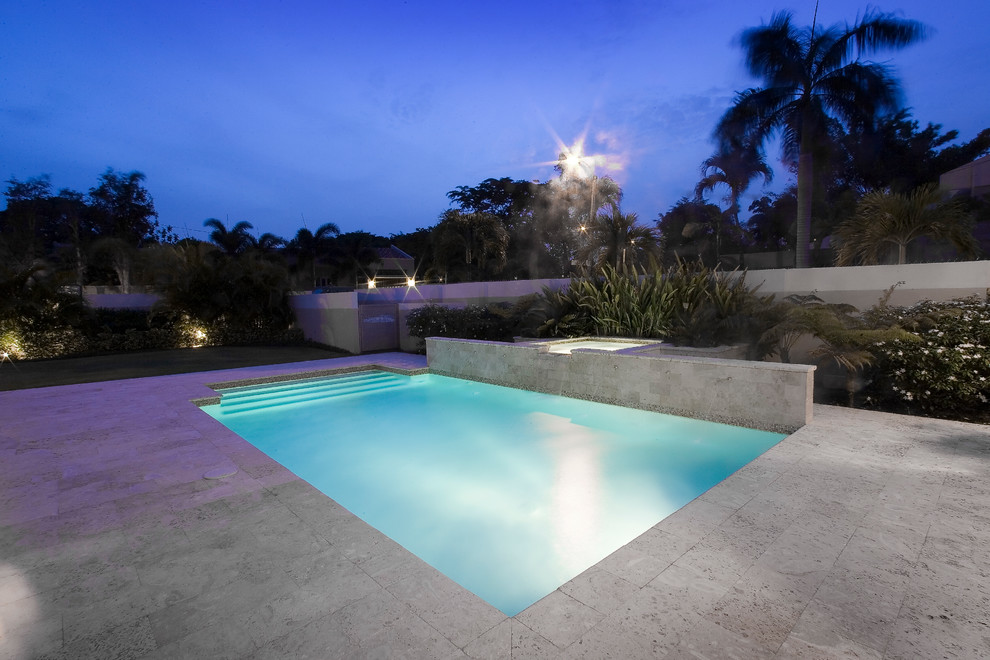 Réalisation d'une grande piscine latérale design rectangle avec un point d'eau et des pavés en pierre naturelle.