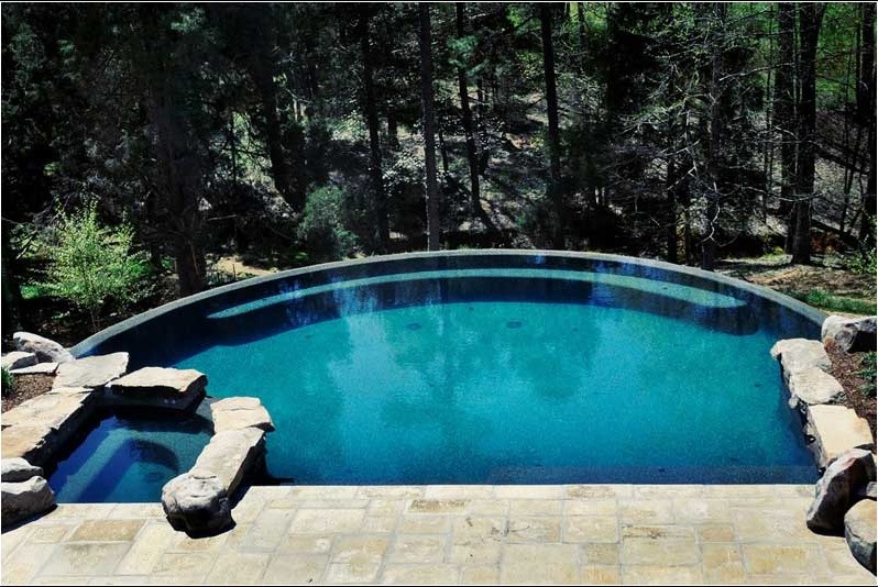 Aménagement d'une piscine arrière et à débordement campagne de taille moyenne et sur mesure avec un point d'eau et des pavés en béton.