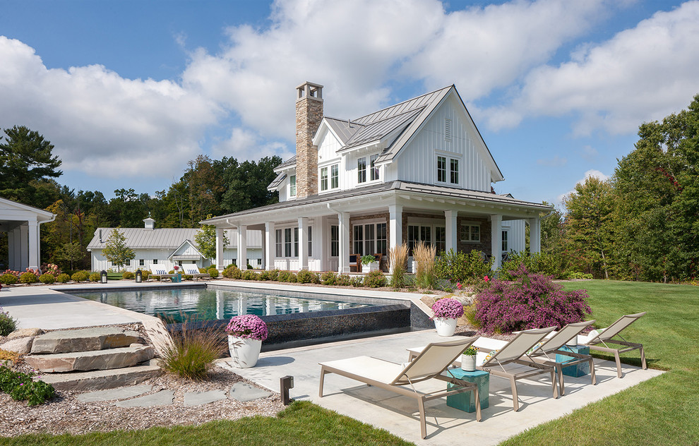 Diseño de piscina infinita de estilo de casa de campo rectangular en patio trasero con losas de hormigón