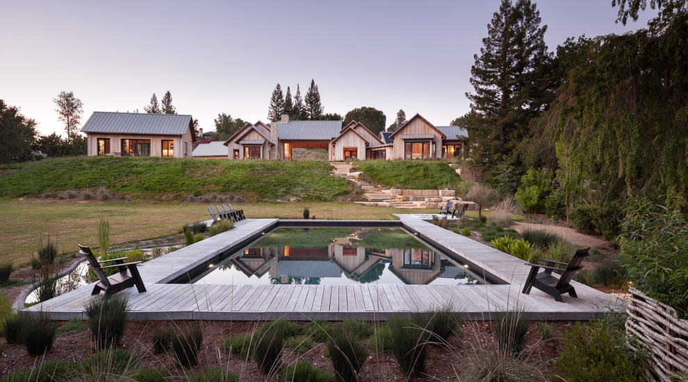 Ejemplo de piscina de estilo de casa de campo extra grande rectangular en patio trasero con entablado