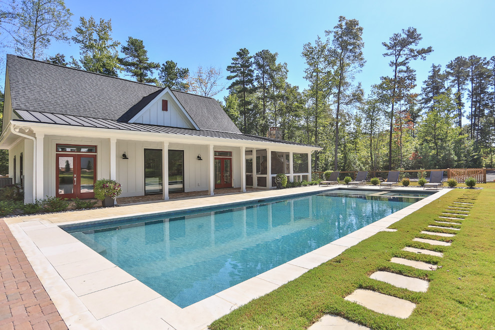 Modelo de casa de la piscina y piscina alargada de estilo de casa de campo extra grande rectangular en patio trasero con suelo de hormigón estampado