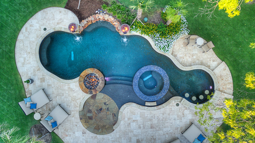 Foto di una grande piscina tropicale a "C" dietro casa con una vasca idromassaggio e piastrelle