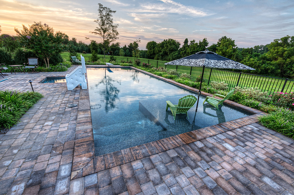 Réalisation d'une grande piscine naturelle et arrière marine rectangle avec un bain bouillonnant et des pavés en brique.