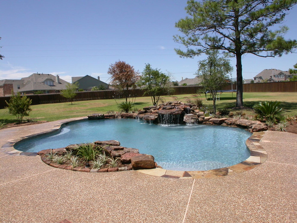 Exempel på en stor klassisk anpassad pool på baksidan av huset, med en fontän och stämplad betong
