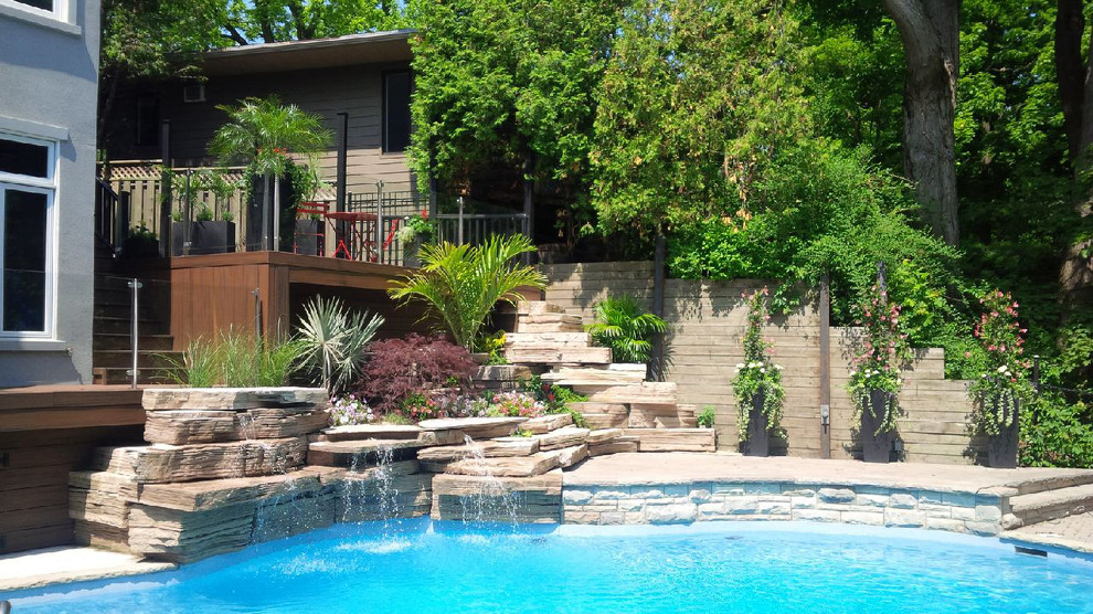 Foto de piscina con fuente tropical en patio trasero con adoquines de piedra natural