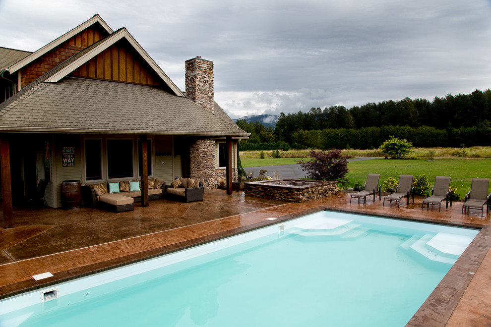 Diseño de piscina alargada de estilo de casa de campo grande rectangular en patio trasero con suelo de hormigón estampado