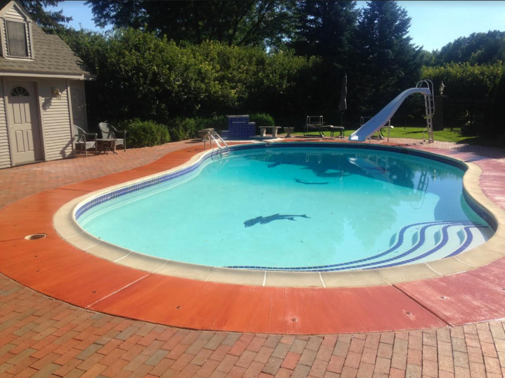Foto de piscina con tobogán clásica de tamaño medio tipo riñón en patio trasero con adoquines de ladrillo