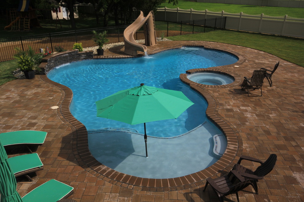 Diseño de piscina exótica grande a medida en patio trasero con adoquines de hormigón