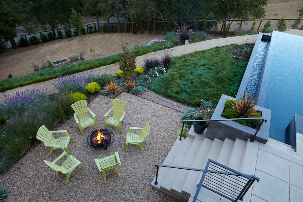 Diseño de piscina infinita moderna grande rectangular en patio trasero con adoquines de piedra natural