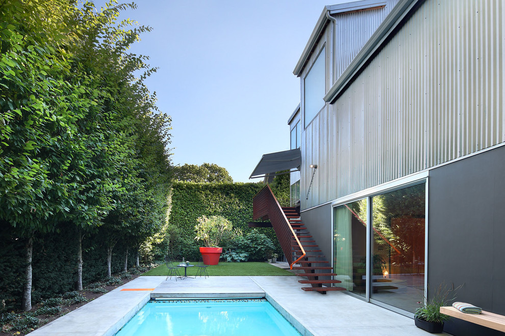 Immagine di una piscina monocorsia design rettangolare di medie dimensioni e dietro casa con lastre di cemento