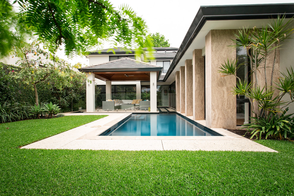 Modelo de casa de la piscina y piscina tropical rectangular en patio trasero con losas de hormigón