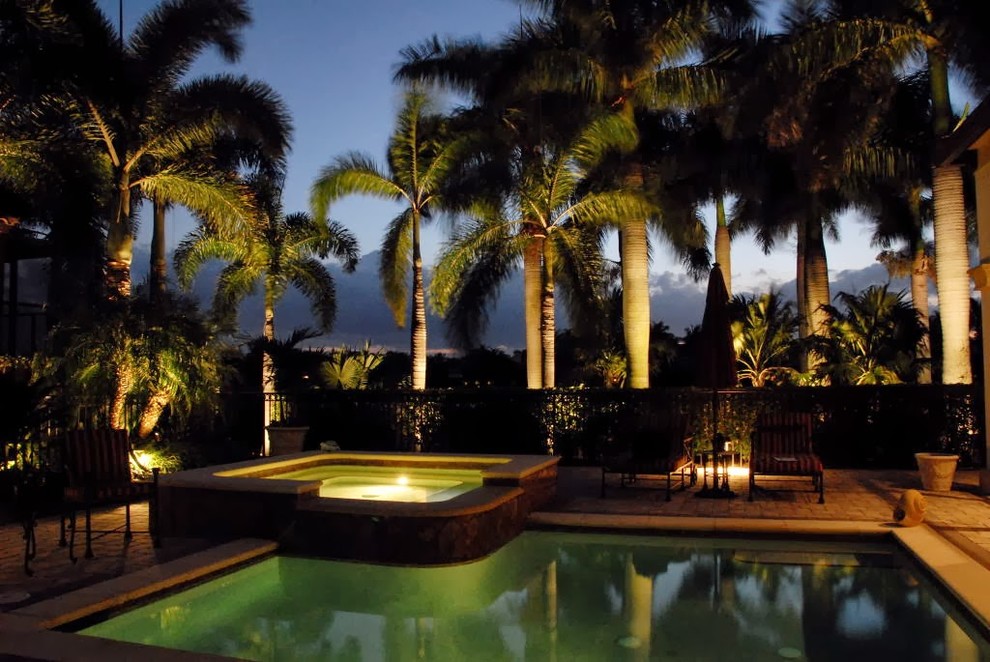 Modelo de piscina con tobogán infinita tropical de tamaño medio a medida en patio trasero con adoquines de piedra natural