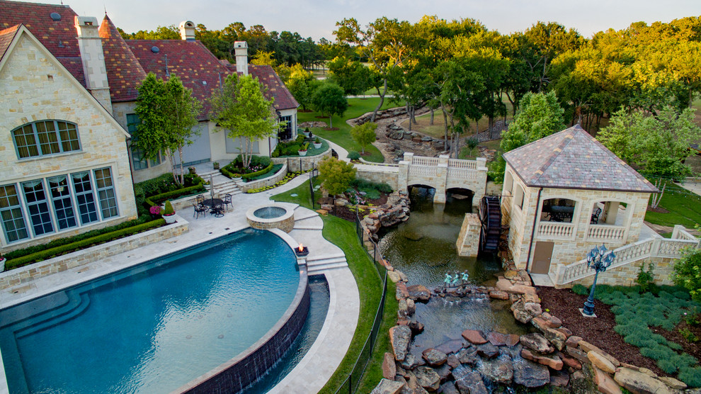 На фото: огромный бассейн-инфинити произвольной формы на заднем дворе в стиле неоклассика (современная классика) с фонтаном и покрытием из каменной брусчатки