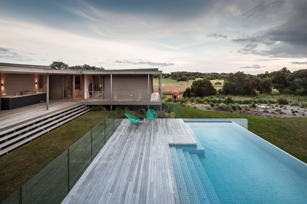 Cette photo montre une grande piscine à débordement tendance sur mesure avec une terrasse en bois.