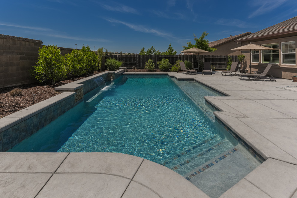 Modelo de piscina con fuente tradicional grande rectangular en patio trasero con adoquines de piedra natural