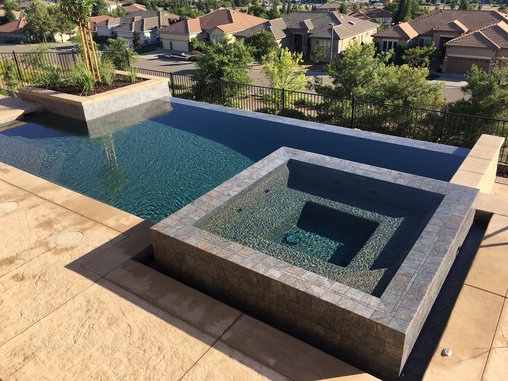 Cette photo montre une piscine à débordement et arrière tendance de taille moyenne et rectangle avec un bain bouillonnant et du béton estampé.