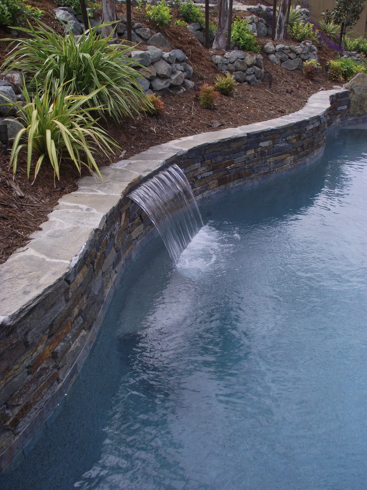 Ejemplo de piscina con fuente exótica de tamaño medio tipo riñón en patio trasero con adoquines de piedra natural