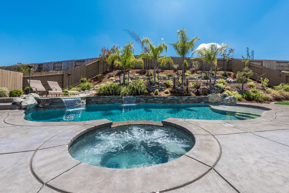 Imagen de piscina con fuente tropical de tamaño medio tipo riñón en patio trasero con adoquines de piedra natural