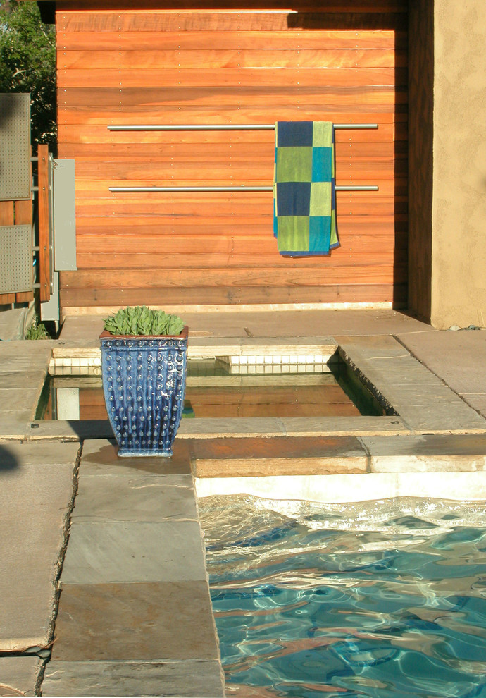 Immagine di una piscina design rettangolare dietro casa con pavimentazioni in pietra naturale e una vasca idromassaggio