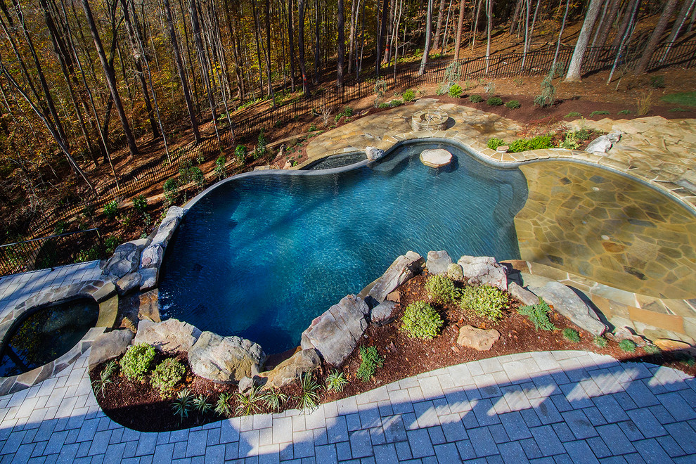 На фото: большой бассейн-инфинити произвольной формы на заднем дворе в стиле рустика с фонтаном и покрытием из каменной брусчатки