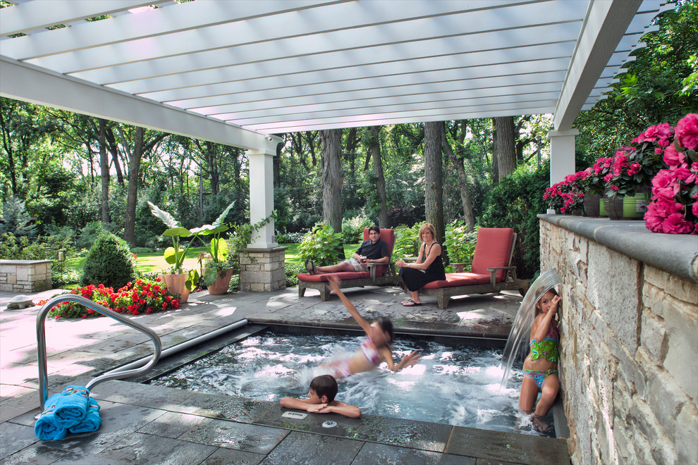 Foto de piscina alargada clásica grande rectangular en patio trasero con adoquines de piedra natural y paisajismo de piscina
