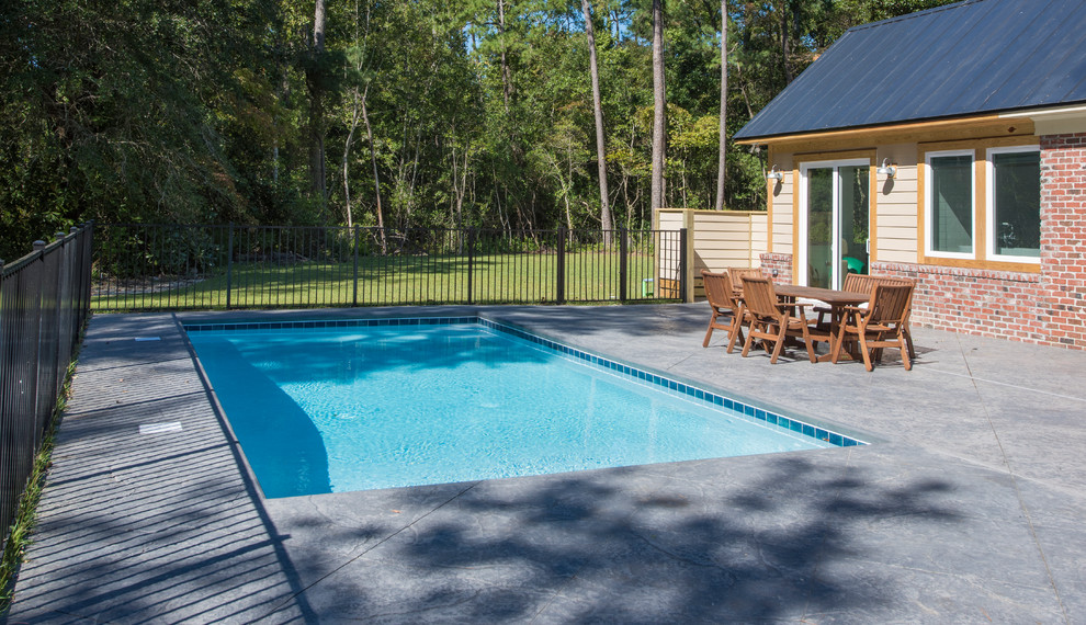 This is an example of a medium sized traditional back rectangular lengths swimming pool in Raleigh with a pool house and concrete slabs.