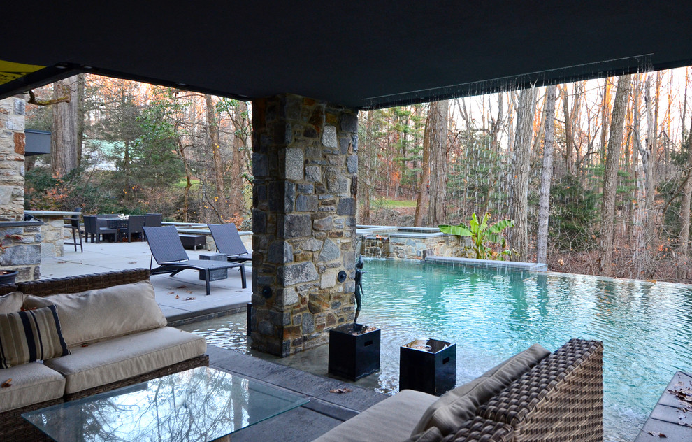 Esempio di un'ampia piscina a sfioro infinito design personalizzata dietro casa con una vasca idromassaggio e lastre di cemento