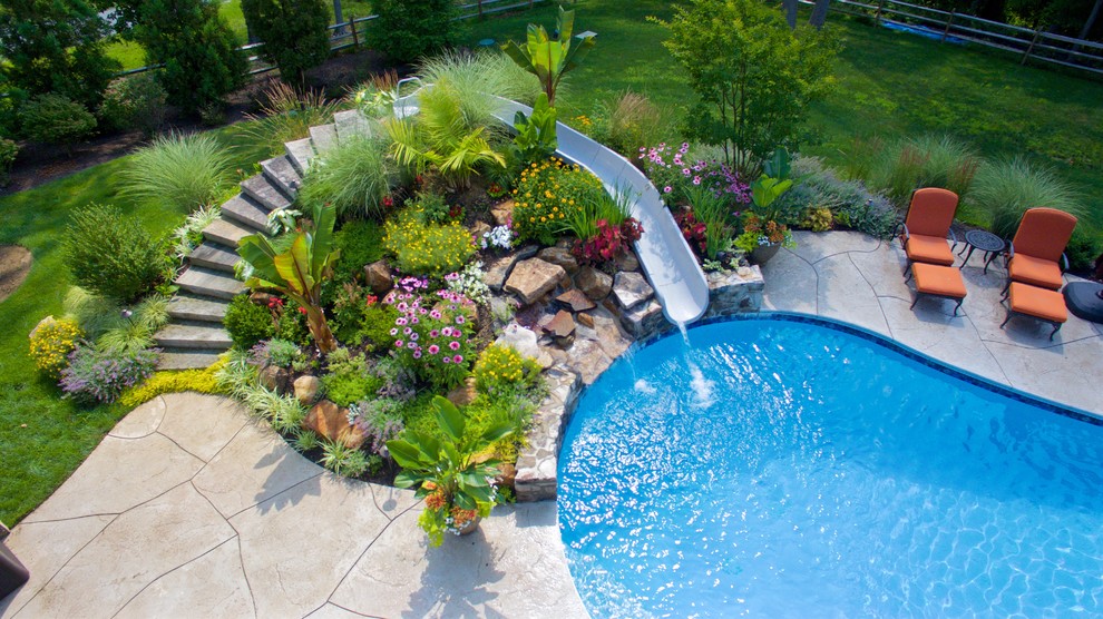 Immagine di una grande piscina design personalizzata dietro casa con un acquascivolo e cemento stampato