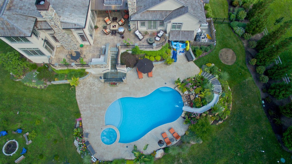 Diseño de piscina con tobogán actual grande a medida en patio trasero con suelo de hormigón estampado