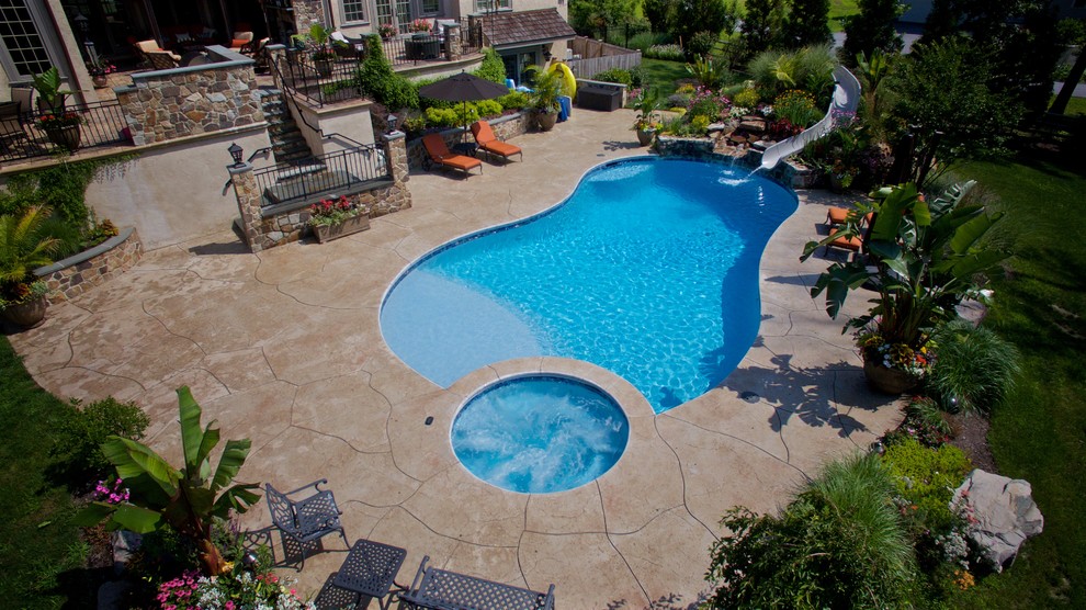 Ejemplo de piscina con tobogán contemporánea grande a medida en patio trasero con suelo de hormigón estampado