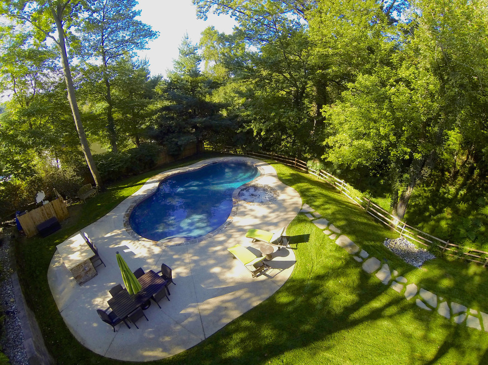 Modelo de piscina natural rústica de tamaño medio a medida en patio trasero con losas de hormigón