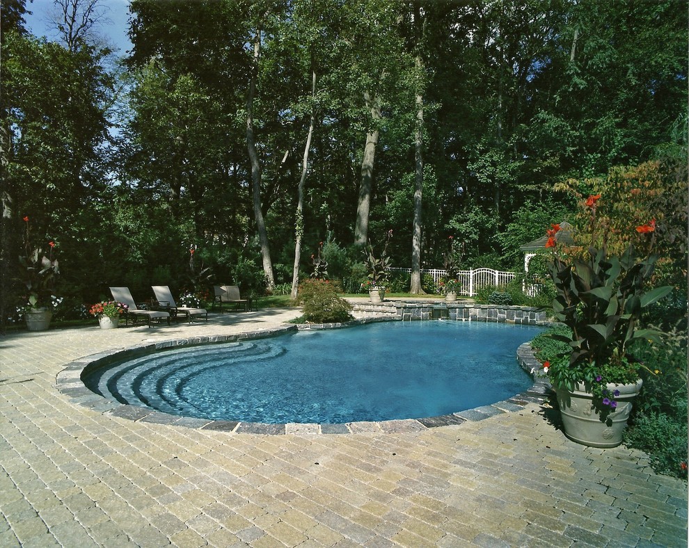 Modelo de piscina natural tradicional grande a medida en patio trasero con adoquines de ladrillo