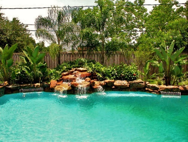 Large modern back custom shaped swimming pool in Houston with a water feature and stamped concrete.