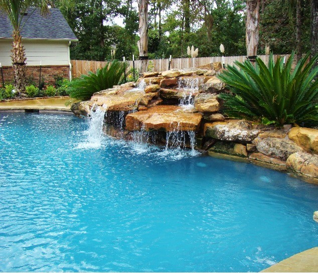 Modelo de piscina con fuente moderna grande a medida en patio trasero con suelo de hormigón estampado