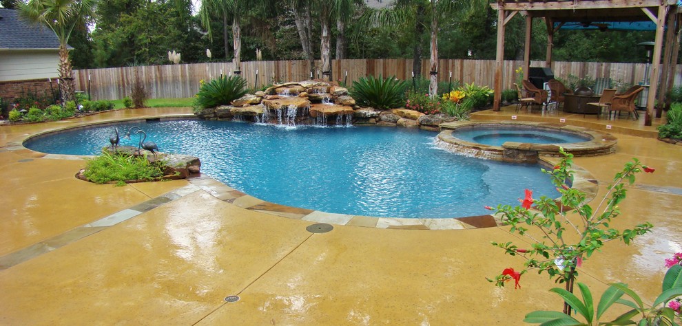 Photo of a large modern back custom shaped swimming pool in Houston with a water feature and stamped concrete.