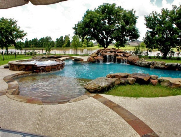 This is an example of a large modern back custom shaped swimming pool in Houston with a water feature and stamped concrete.