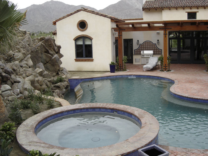 Cette photo montre une grande piscine naturelle et arrière méditerranéenne sur mesure avec des pavés en brique et un bain bouillonnant.