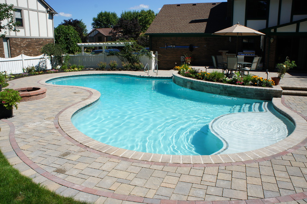 Imagen de piscina clásica de tamaño medio tipo riñón en patio trasero con adoquines de hormigón